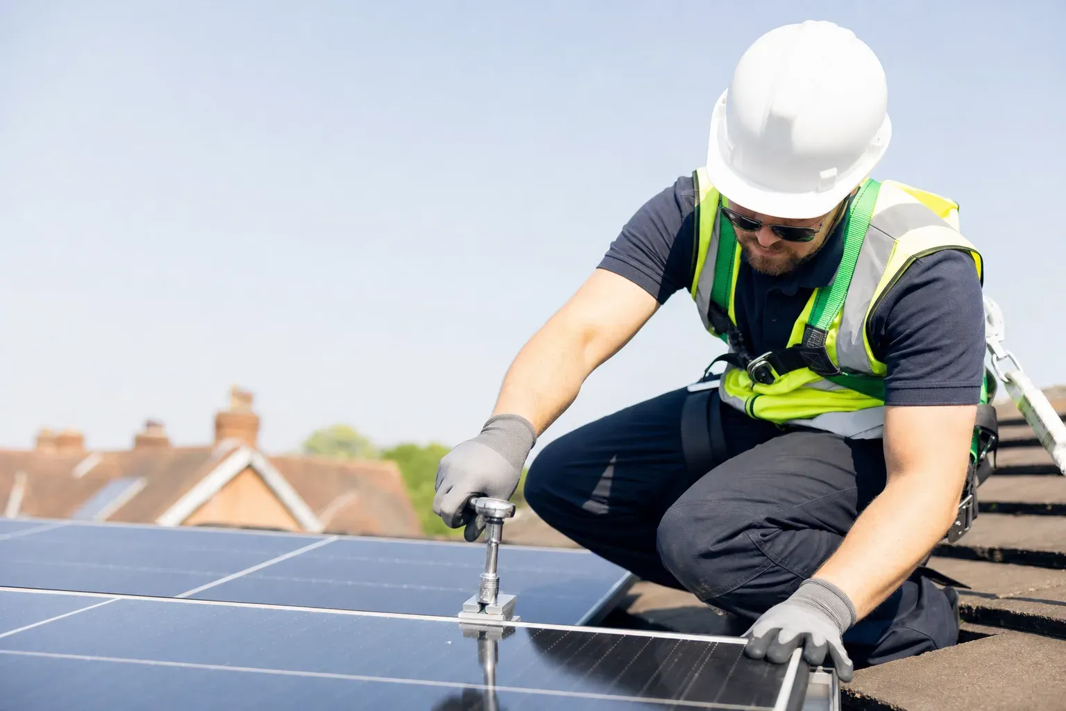 An installer in a harness securing a solar panel to a mounting rail on a UK roof.